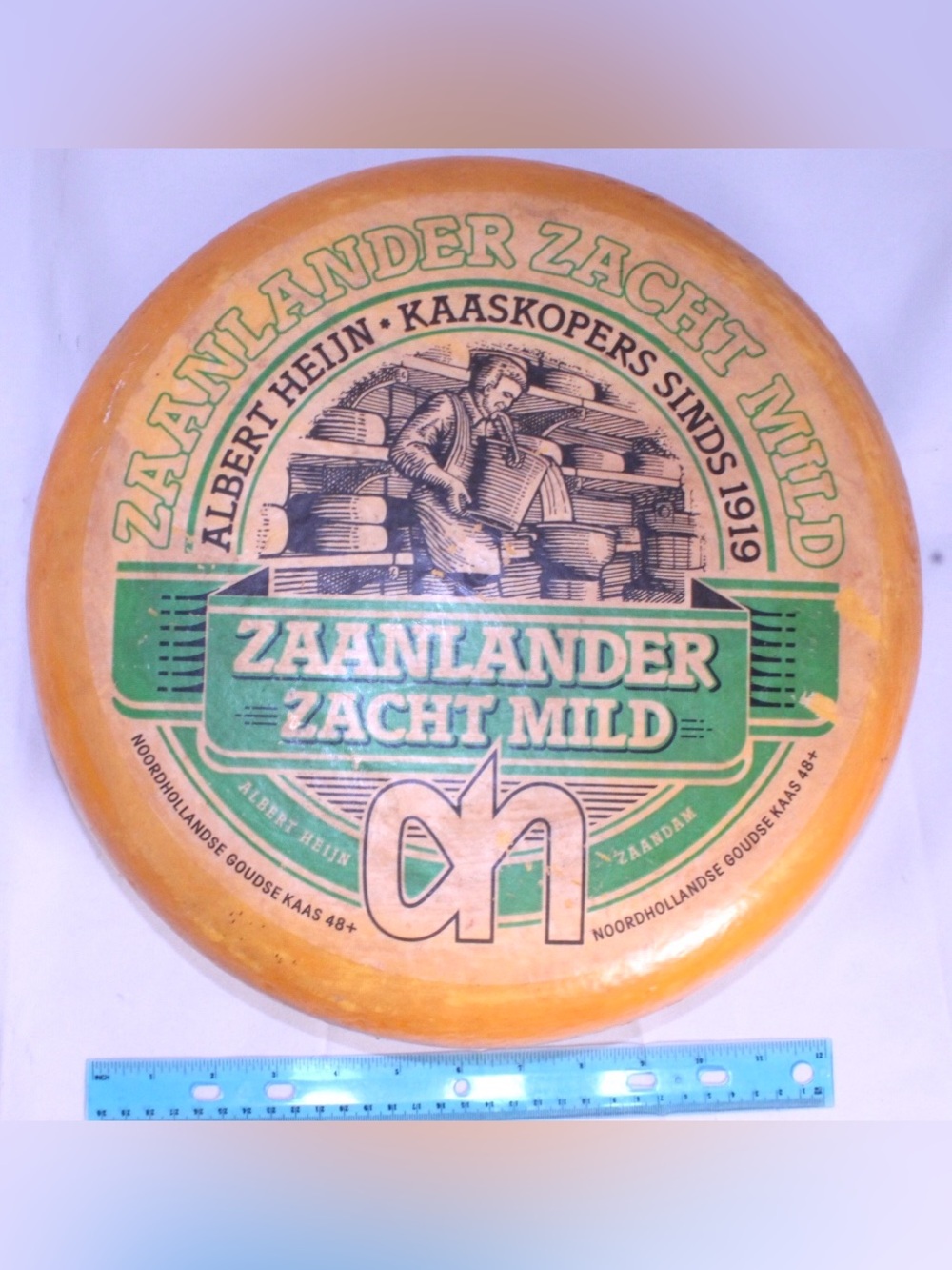 Plastic Zaanlander Zacht Mild Dutch Cheese Wheel - Orange & Green Advertisement